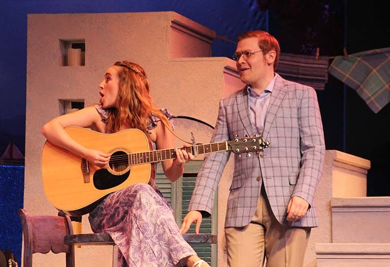 Lauren Mary Moore playing acoustic guitar with cast member during scene of Momma Mia