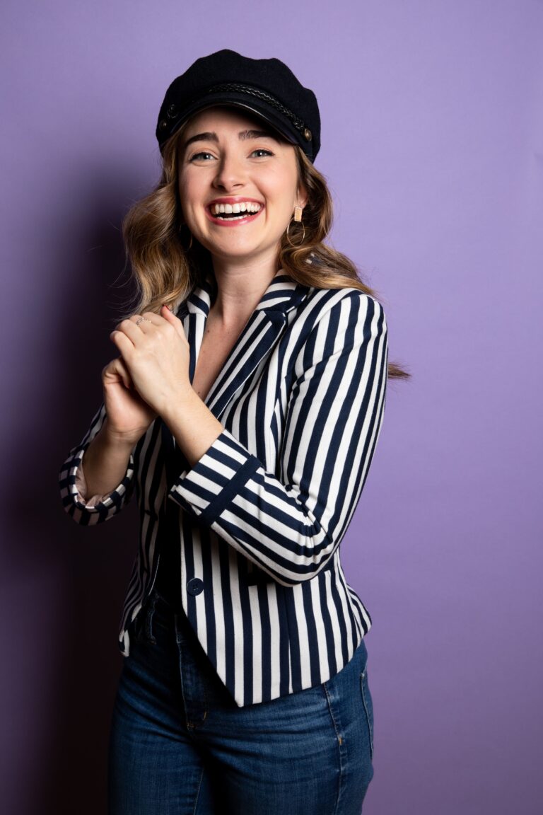 Lauren Mary Moore in striped jacket with hat against purple wall
